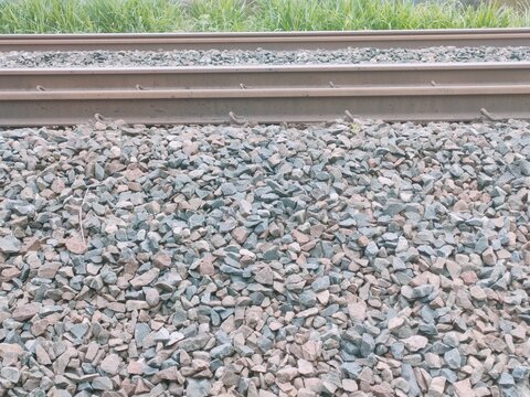 Close up of railroad ballast gravel texture with steel railway tracks. Concept of transportation infrastructure, public transit, and industrial construction background