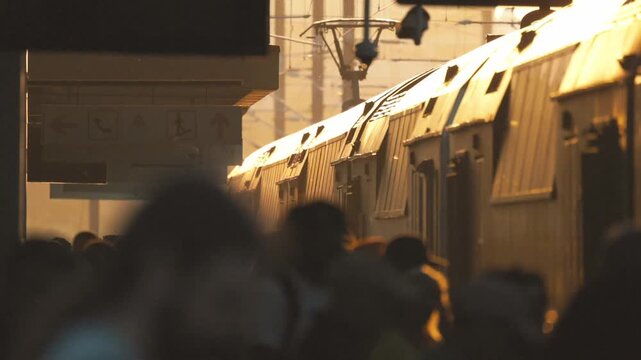 Morning crowd at a busy train station in the city during rush hour with sunlight shining on arriving trains