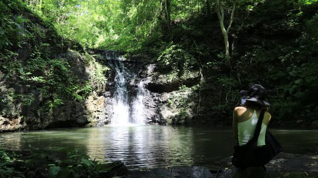 The video background features a natural landscape of a waterfall in a lush forest. Sam Lan Waterfall in Saraburi National Park boasts beautiful flowing water surrounded by diverse flora.