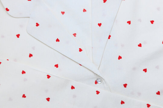 Red hearts on white fabric create a pattern on a button up shirt laid flat on a surface
