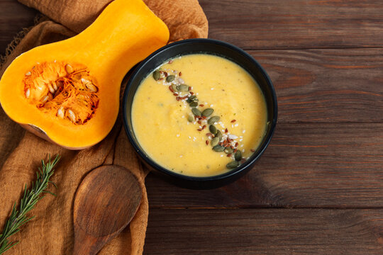Pumpkin cream soup served in bowl with raw pumpkin on wooden table with spoon and cloth around