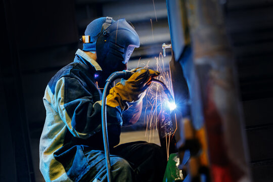 Welder operating welding torch on metal structure in workshop, recovery work for excavator bucket