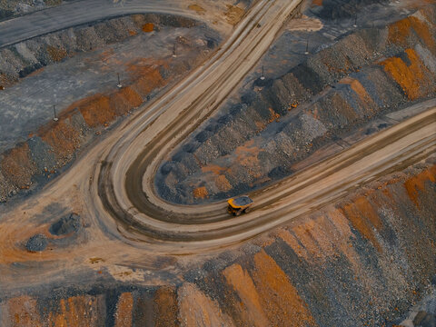 Mining haul truck navigating curved road in open pit quarry, gold mining industry aerial view