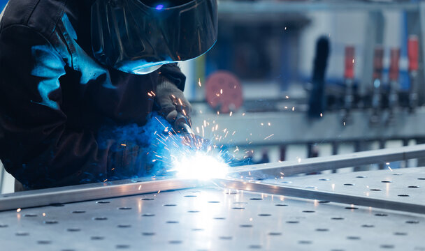 Welder performing arc welding on steel worktable in factory