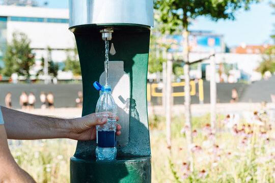Hand refilling plastic water bottle at public drinking fountain, close-up