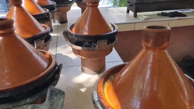 Steaming Moroccan tagines cooking over hot charcoal, with rising smoke and rustic clay pots creating an authentic traditional food scene, in the Ourika Valley, near Marrakesh, Morocco.