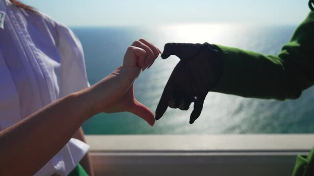 Heart hands sea two people forming a heart shape with their fingers against a sparkling ocean horizon on a sunny day
