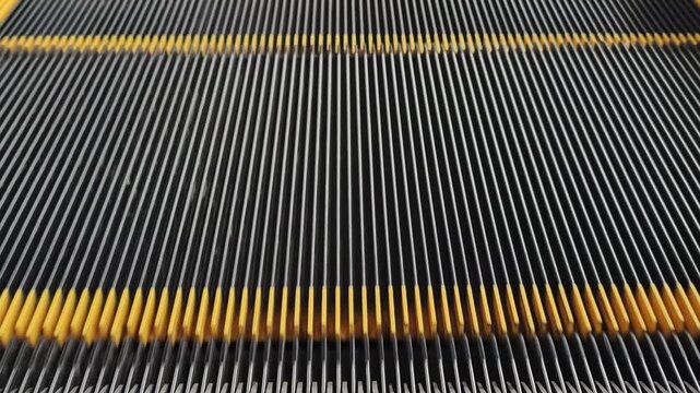 Close-up of escalator grooved metal steps moving rhythmically with yellow safety demarcation lines. The endless mechanical motion creates an abstract industrial background.
