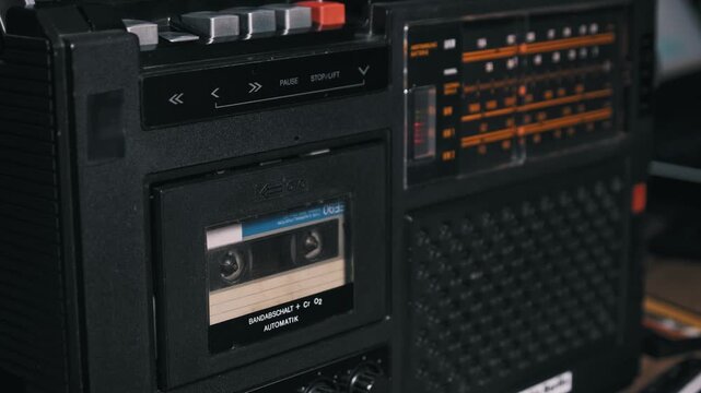 A male hand presses the eject button on a retro black boombox and removes the audio cassette tape. Concept of obsolete technology, 80s nostalgia, and listening to classic music.