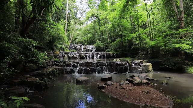 The video background features a natural landscape of a waterfall in a lush forest. Sam Lan Waterfall in Saraburi National Park boasts beautiful flowing water surrounded by diverse flora.