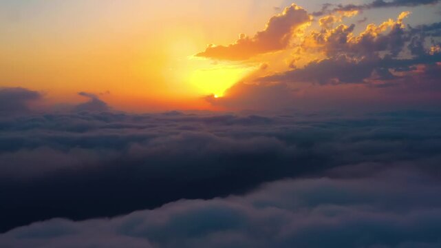 Cinematic aerial view above dense white cloud layer during vibrant orange sunset at high altitude.