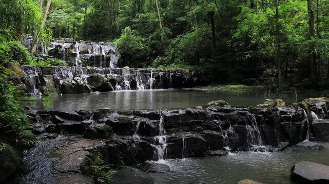The video background features a natural landscape of a waterfall in a lush forest. Sam Lan Waterfall in Saraburi National Park boasts beautiful flowing water surrounded by diverse flora.