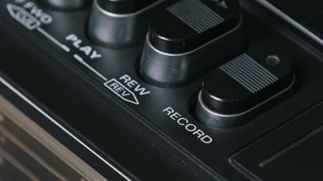 Macro side angle shot of a finger pushing the record control on a vintage cassette recorder. The ridged button and dusty panel highlight the old school audio equipment.