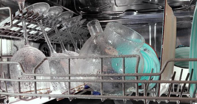 Water spraying inside modern dishwasher cleaning crystal glasses and ceramic plates during washing cycle process.