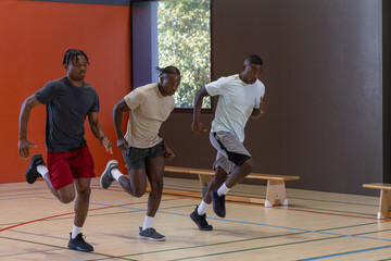 Fototapeta premium Three adult males sprinting on hardwood gym court in athletic shoes by wooden benches