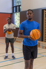 Naklejka premium Two African American men practicing on gym court wearing blue and beige holding basketballs