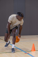 Naklejka premium Basketball player is dribbling orange ball on wood court with painted lines near bright orange cone