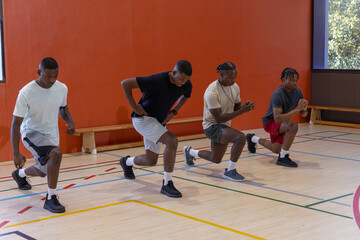 Fototapeta premium African American men performing forward lunges on wooden court with court lines, bench, sneakers