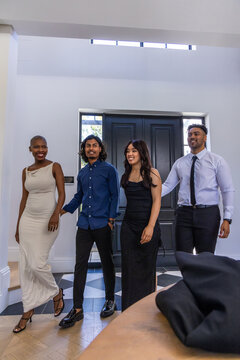 Diverse friends walking through bright entry toward camera, wearing formal attire by dark doors