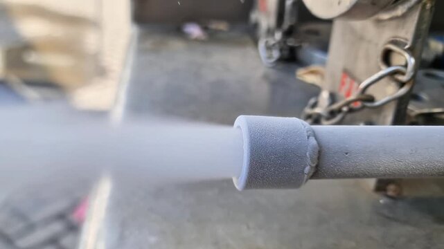 Industrial venturi injector nozzle releasing high-pressure white vapor and mist in a factory setting.