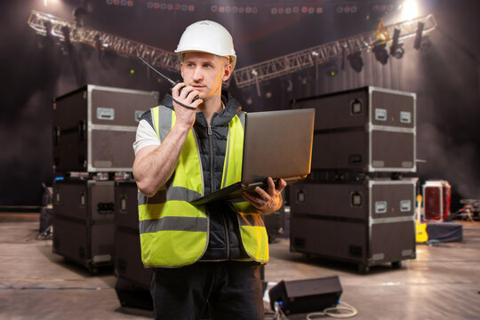 Event production management, stage technician coordinates concert equipment with radio and laptop during live show setup.