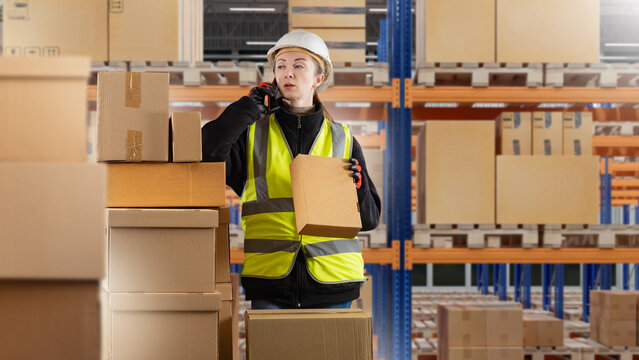 Warehouse logistics, Female worker handles cardboard boxes and talks by phone inside a large storage distribution center.