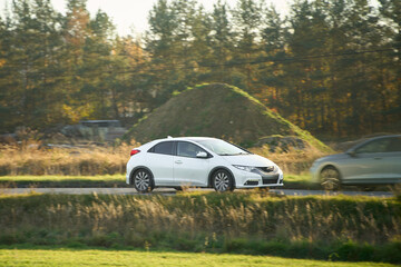 Fototapeta premium White compact hybrid car driving on country road in autumn