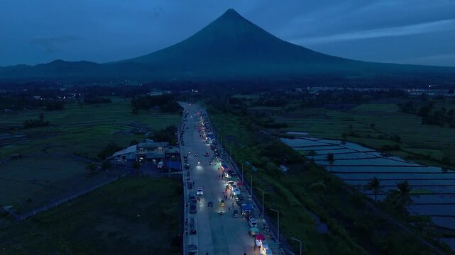 Majestic Mayon Volcano at dusk with illuminated new road and rice fields, Albay, Philippines.