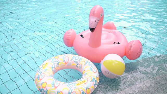 Pink flamingo pool float with swim ring and beach ball in swimming pool