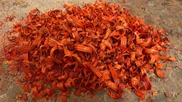 Curly, orange-red wood shavings from padauk piled on a workshop floor.
