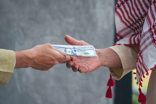 Close up Two Islamic man hands giving USD money Financial Bill. Men hands muslim dress modern uae city pay debt Exchanging Savings Wages Financial Loan Spending Money. Arab men wear hijab Headscarf