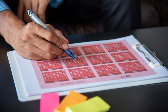 Calendar plan event. Close up man Hands using pen note 2027 event planner timetable agenda plan schedule event. Man planner agenda organizer schedule. 2026 Calendar desk objects on office table