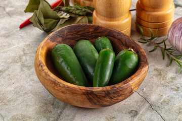 Fresh green jalapeno peppers in rustic wooden bowl with herbs and spices