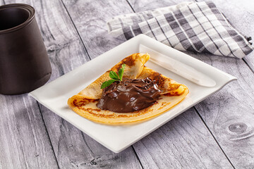 Pancake with chocolate spread and mint leaf on white plate © Andrei Starostin