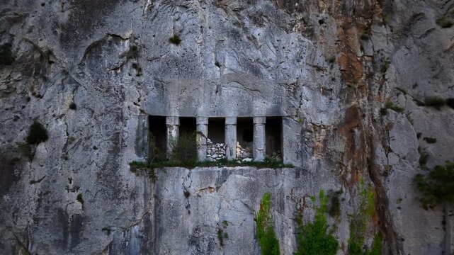 4K 60fps drone slowly pulling back from a close-up of an ancient rock-cut cliff tomb, revealing the wider landscape in a smooth cinematic reveal shot.