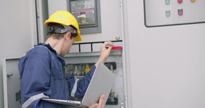 A skilled electrical engineer performs system diagnostics, inspecting and operating a high-voltage industrial control panel for quality control and maintenance.