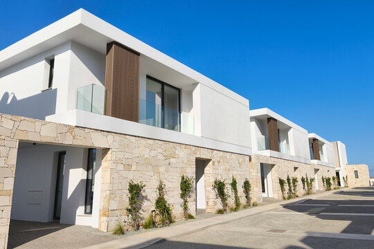 Modern luxury villas with minimalist architecture, natural stone walls, and expansive glass windows in a premium residential community under a bright blue sky.