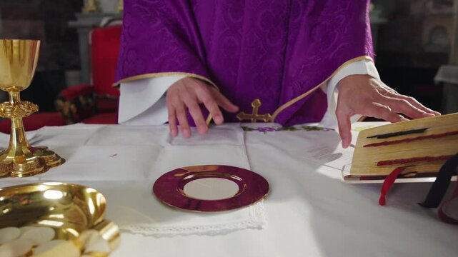 Catholic priest leading the Eucharist Liturgy, reading from the liturgical book placed on the altar with sacred vessels, chalice, and paten.