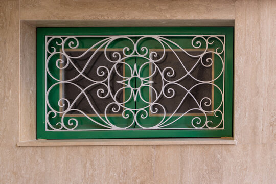 Decorative Green Window With Ornamental White Metal Grille Set in Beige Stone Wall