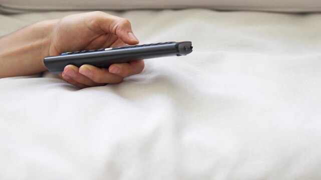 Man&rsquo;s hand with hangnails holding and pressing buttons on a television remote while relaxing on a sofa at home
