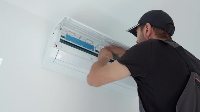 Man cleans a blue filter inside an open wall air conditioner indoors. Concept of AC maintenance filter cleaning and cooling service.