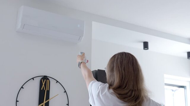 Woman uses a remote control to turn on a wall air conditioner at home. Concept of home cooling room temperature and indoor comfort.
