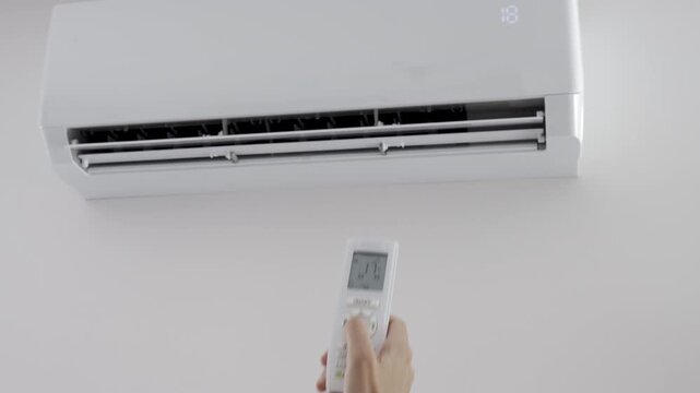 Person adjusts air conditioner temperature with a remote control in a room. Concept of cooling summer heat and climate control.