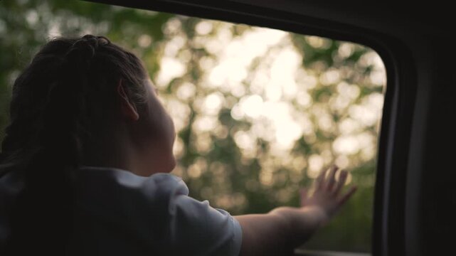 Child enjoying car travel with family. Happy child look out window. Sunset on girl face Family road trip moment. Child joyful travel experience. Window view during travel. Girl looking out car window