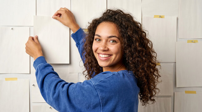 young woman with curly hair organizing blank papers on a wall, concept of planning and creativity