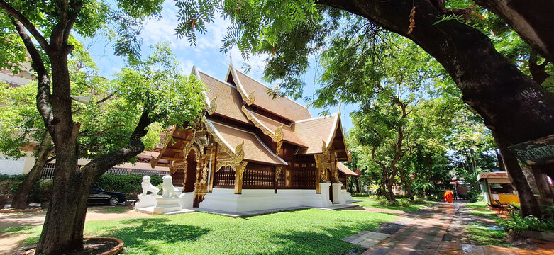 Historic Lanna-style temple architecture at Wat Phra Singh under a clear blue sky, surrounded by lush green trees in Chiang Mai, Thailand.