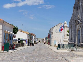 Obraz premium The main street of the Citadel of Brouage, its shops, cafés and bourgeois homes lined with flowers between the Saint-Pierre church of Brouage and the Royal Forge before Royal Gate