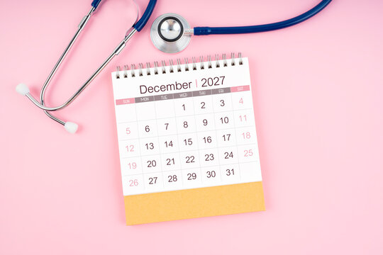December 2027 desk calendar and Medical stethoscope on  pink background.