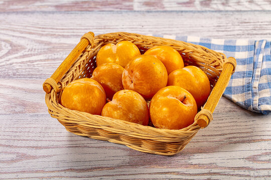 Golden yellow plums in wicker basket on rustic wooden table with checkered napkin