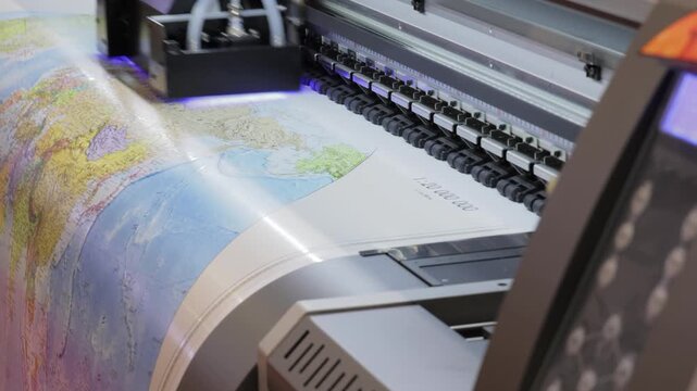 Industrial large format inkjet printer printing detailed world map on vinyl roll in professional workshop.